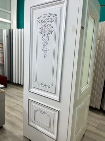 Ağ rəngdə, oyma naxışlı qapı. Qapının üzərində dekorativ çərçivələr və