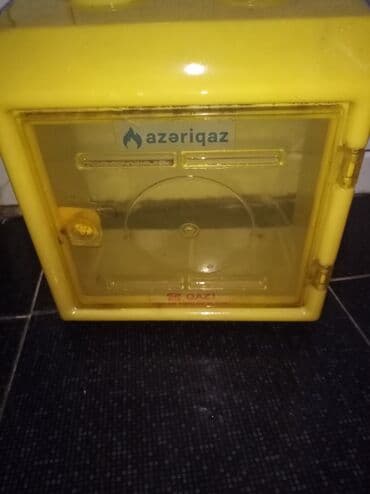 Sarı rəngdə, şəffaf qapaqlı qaz sayğacı qutusu. Qutu qaz sayğacını