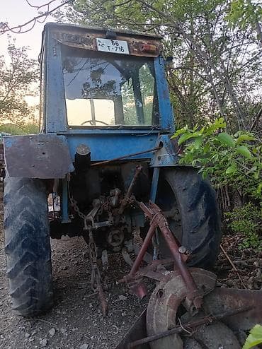 Mavi rəngli kabinəli təkərli traktor. Arxa hissədə üçnöqtəli asqı