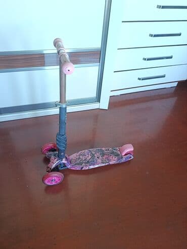 трюковой самокат: Çəhrayı rəngdə və qara naxışlı, üç təkərli uşaq skuteri. Skuterin — 2