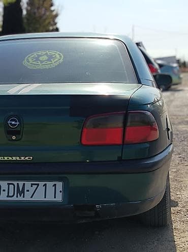 Opel sedan – yaşıl rəng, 4 qapılı, arxa çəkiliş emblemli model. Xarici