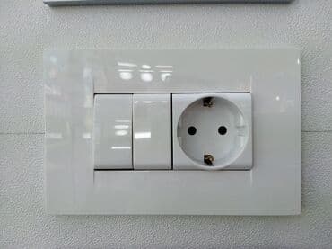 Ağ rəngdə olan, divara quraşdırılmış elektrik rozetkası və açarı