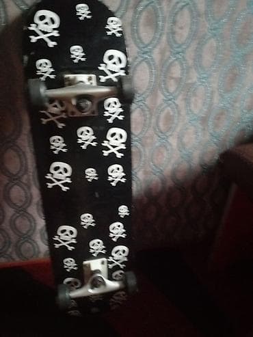 Skateboard – qara rəngli gövdə, üzərində ağ kəllə‑sümük naxışları. -