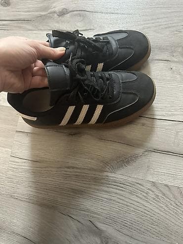 Kişi ayaqqabıları: Qara rəngli idman ayaqqabısı, üç ağ zolaqlı klassik dizayn. Üst hissə — 4