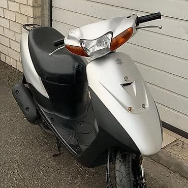 18 disk təkər: Gümüşü rəngdə, qara detallarla bəzədilmiş Suzuki skuter. Bu model — 2