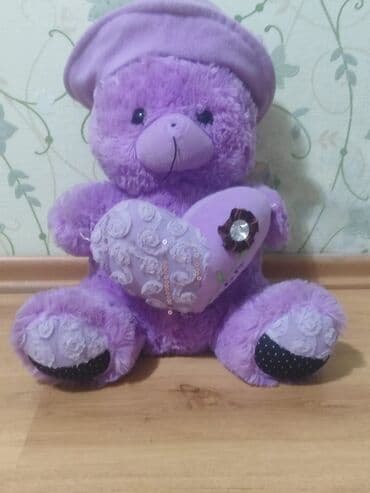 Bənövşəyi rəngdə, şapka və ürək formalı yastıq tutan yumşaq oyuncaq