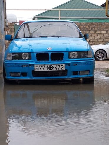 Mavi rəngli, dördqapılı BMW avtomobili. Avtomobilin ön hissəsində qara