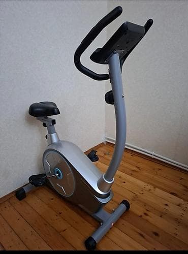 Gümüşü rəngdə, qara oturacağı və tutacaqları olan stasionar velosiped