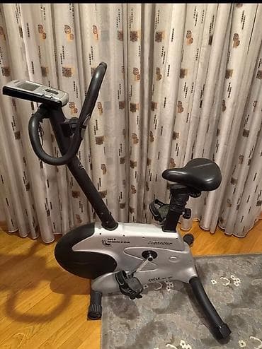 Evdə idman üçün nəzərdə tutulmuş boz rəngli məşq velosipedi. Bu