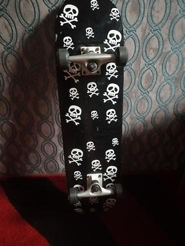 Skateboard – qara rəngli gövdə, üzərində ağ kəllə‑sümük naxışları. -