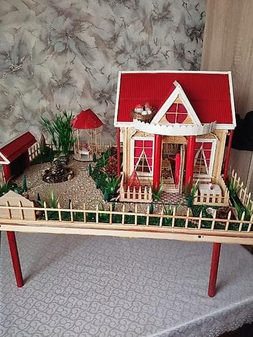 Miniatür ev modeli, qırmızı damı və ətrafında hasarlı yaşıllığı ilə